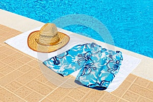 Hat and swimming trunks on towel near swimming pool