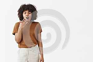 Hate jetlag. Portrait of sleepy cute African American woman with afro hairstyle closing eyes and yawning with wide