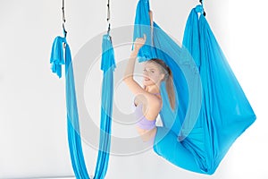 Hatha aero fly yoga concept. Beautiful young female trainer showing stretching exercises on blue hammock in white studio