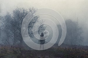 A haunted figure on a path on a hill on a moody, foggy winters day. With an abstract, grain, grunge edit