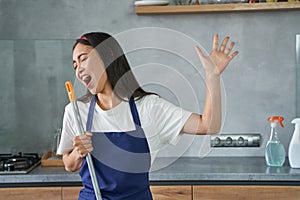 Have fun. Portrait of joyful young woman, cleaning lady pretending to sing, holding broom while cleaning the floor