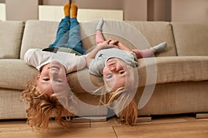 Have fun. Portrait of playful kids, little boy and girl lying upside down on a sofa in the living room