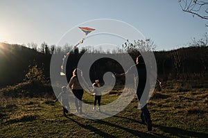 Have fun spending time with two children outdoors in nature. Rear view. Young parents with son and daughter run across field at