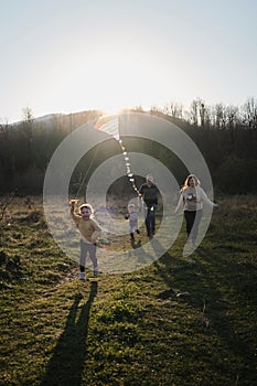 Have fun spending time with two children outdoors in nature. Young Caucasian parents with their son and daughter run across field