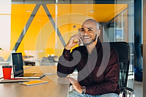 Have a nice working day. Confident young african american businessman working on laptop and talking on cell phone while sitting at