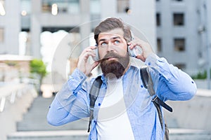 We have our ears in the streets. Bearded man wear ear phones outdoors. Hipster listen to music in headphones