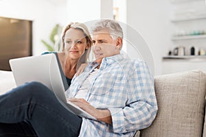 They have a strong connection. an affectionate mature couple using a laptop while sitting on the sofa together at home.