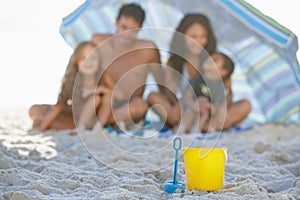 Having buckets of fun at the beach. A happy family smiling while sitting under an umbrella at the beach with a spade and