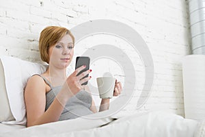 Having coffe breakfast on bed while watching internet news in his mobile phone in online communication