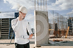 Having conversation by the phone. Man in uniform is working on the construction site