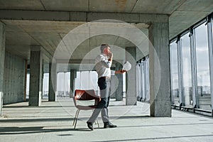 Having conversation by using phone. Young man in formal wear is working indoors on the construction