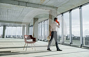 Having conversation by using phone. Young man in formal wear is working indoors on the construction