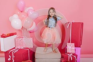 Having fun of cute pretty birthday kid in tulle skirt dancing on chair suround a lot of giftboxes, balloons  on