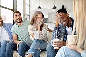 Having fun with friends. Group of young multiracial people drinking coffee at home, joking and laughing together