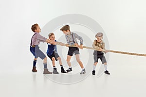 Having fun. Group of little boys, children playing together, pulling the rope over grey studio background. Concept of