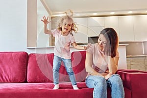 Having fun and jumping. Young mother with her little daughter in casual clothes together indoors at home