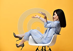 Having fun stylish woman in pantsuit sitting in armchair holding on her open palms at arms length or juggling something