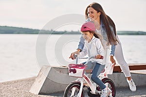 Having fun together. Mother with her young daughter is with bicycle outdoors together