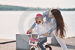 Having fun together. Mother with her young daughter is with bicycle outdoors together