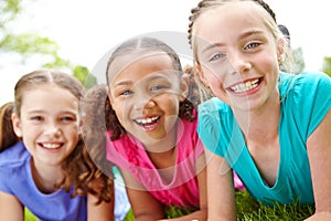 Having fun together. Three multi-ethnic young girls lying on the grass in a park smiling at the camera.