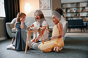 Having fun. A young woman with two girls is playing a wooden tower game indoors together