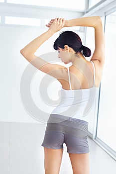 Having a good stretch. Young fit woman stretching while indoors - rear view.