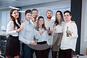 Having good time. Photo of young team in classical clothes holding drinks in the modern good lighted office