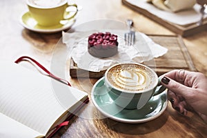 Having lunch with coffee flat white and sweet chocolate cookie in a cafe or restaurant. Woman hand holds a green cup. photo