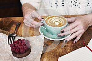 Having lunch with coffee flat white and sweet chocolate cookie in a cafe or restaurant. Woman hands holds a green cup. Hipster photo