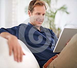 Having a really relaxed day...a handsome man using his tablet while sitting on the sofa at home.