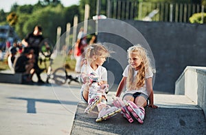 Having a rest. On the ramp for extreme sports. Two little girls with roller skates outdoors have fun