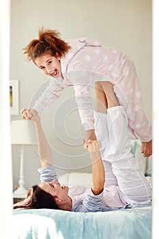 Having some bedtime fun. Shot of a young mother lifting her daughter with her legs while lying on bed.