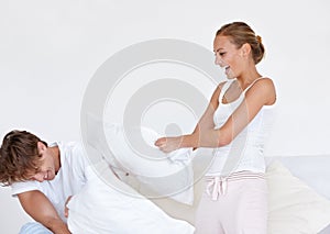 Having some fun. A young couple wearing pjamas and having a pillow fight together.