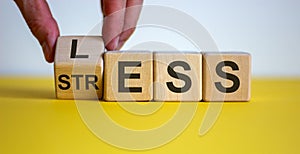 Having less stress or being stress-less. The word `STRESS` and `LESS` on wooden cubes. Male hand.  Beautiful yellow table, whi