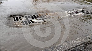 Havy rain in a city, flooded street and manhole cover of storm drain.