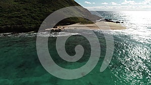 Hawaii, low angle view with drone camera moving forward, camera closing in on beach on green island in open waters, color graded