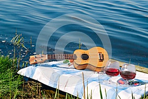 guitar and two red wine glasses, picnic on the lake and summer vacation concept