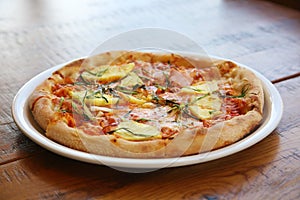 Hawaiian Pizza. A Ham and Pineapple Pizza on a white plate on a wooden table for lunch. Pizza is enjoyed world wide by hungry