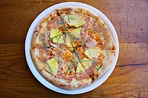 Hawaiian Pizza. A Ham and Pineapple Pizza on a white plate on a wooden table for lunch. Pizza is enjoyed world wide by hungry