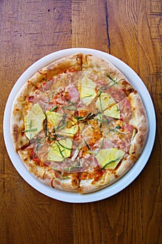 Hawaiian Pizza. A Ham and Pineapple Pizza on a white plate on a wooden table for lunch. Pizza is enjoyed world wide by hungry