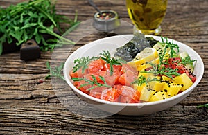 Hawaiian salmon fish poke bowl with rice, avocado, mango, tomato, sesame seeds and seaweeds.