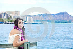 Hawaiian teen with lei sitting by ocean, Waikiki in background