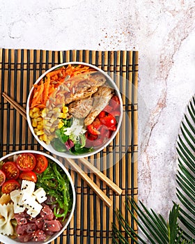 Hawaiian trendy poke bowls, tuna, heura soy protein or vegan chicken, variety vegetables, served in bowl on tropical leaves.