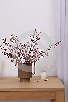 Hawthorn branches with red berries and candle on wooden table indoors