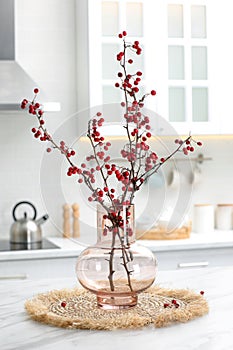 Hawthorn branches with red berries on table in kitchen