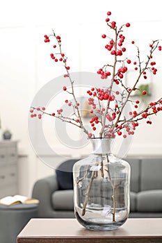 Hawthorn branches with red berries on table in living room