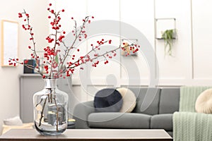 Hawthorn branches with red berries on table in living room, space for text