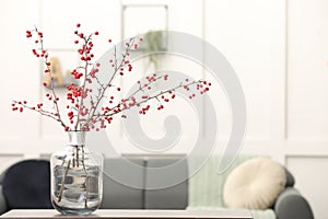 Hawthorn branches with red berries on table in living room, space for text