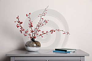 Hawthorn branches with red berries in vase and books on grey table indoors