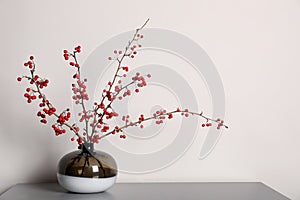 Hawthorn branches with red berries in vase on grey table indoors, space for text